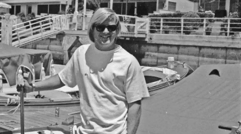 A blonde 'California beach bum' young man in 1972 stands in front of an electric boat