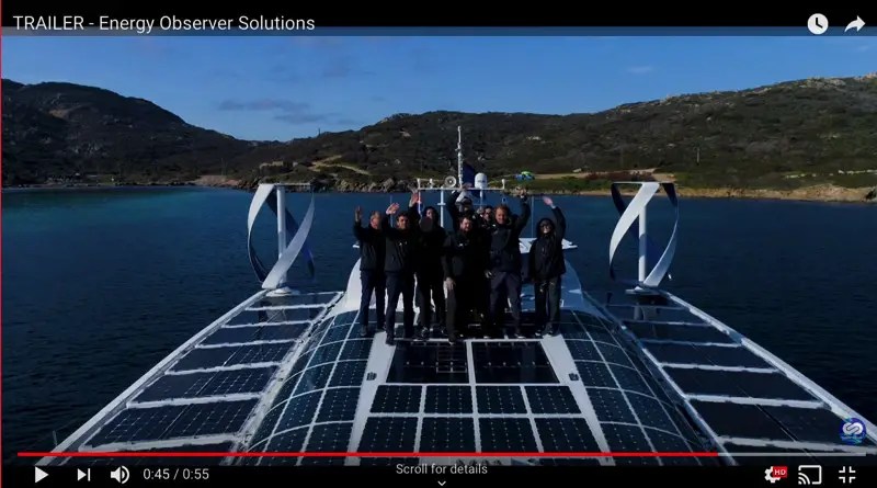 The crew of a 30m boat with the deck covered in solar panels are standing on the deck waving to the camera