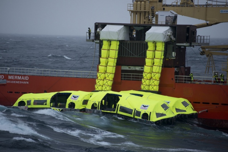 Two e-motor survival boats sit in the water beside a boat with passenger escape chutes leading to them