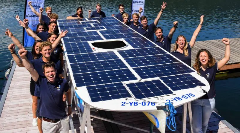 The students of the solar boat team hold up their boat and raise their arms for the camera