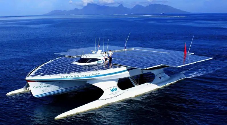 A huge electric ship covered with solar panels sails with mountains n the background