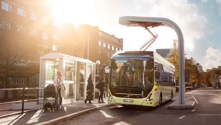 an electric bus on a city street being charged with an overhead system